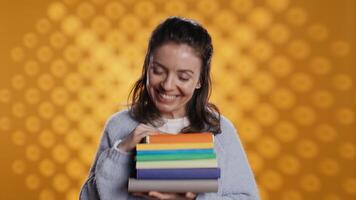 Portrait of happy woman with stack of books in hands showing thumbs up, studio background. Joyous bookworm holding pile of novels, feeling upbeat, doing positive hand gesturing, camera B video