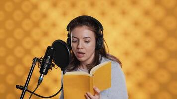 Woman does voiceover reading of book to produce audiobook using dramatic acting. Narrator uses storytelling skills and expressive sounds while producing recording of novel, studio background, camera A video