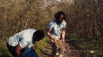 Diverse volunteers collecting garbage and junk from the forest area, fighting environmental pollution and conservation. Group of activists cleaning up the woods, recycling plastic waste. Camera B. video