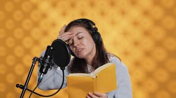 Woman feeling tired while doing voiceover of book and producing audiobook all day. Narrator suffering headache from fatigue, doing digital recording of novel, isolated over studio background, camera A video