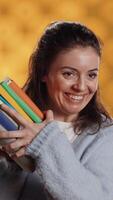 Vertical Excited woman delighted about books ordered, treasuring them, isolated over studio background. Euphoric reading enthusiast cherishing stack of novels, feeling lively and overjoyed, camera A video