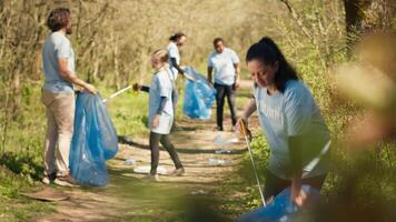 Environmental activist picking up trash with a claw tool and recycling, protecting the natural forest habitat and doing litter cleanup. Woman doing voluntary work to stop pollution. Camera A. video