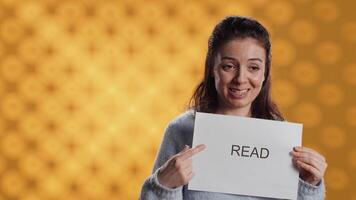 Woman holding message in hands urging people to read more, talking about importance of lecture, isolated over studio background. Bookworm promoting literacy concept, camera A video