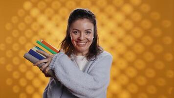 Excited woman delighted about books ordered, treasuring them, isolated over studio background. Euphoric reading enthusiast cherishing stack of novels, feeling lively and overjoyed, camera B video