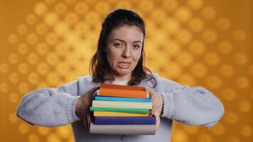 Woman choosing between physical books and ebooks, favoring ereader for lightness, studio background. Bookworm picking digital literature on tablet in front of heavy stack of novels, camera B video