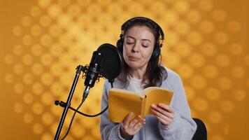 Narrator wearing headphones, reading aloud from book into microphone, exhaling after finally finishing job. Person recording audiobook, creating engaging media content for listeners, camera B video