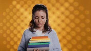 ritratto di ottimista donna Tenere mucchio di libri, godendo lettura passatempo per divertimento scopi. radiante topo di biblioteca con pila di romanzi nel braccia godendo tempo libero volta, studio sfondo, telecamera B video