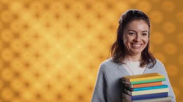 Woman with stack of books in hands throwing apple in air, having fun, living healthy, studio background. Portrait of bookworm holding pile of novels and green fruit, enjoying bio snack video