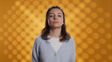 Portrait of relaxed woman posing, looking at camera, isolated over yellow studio background. Caucasian person dressed in casual attire standing, feeling confident, camera B video