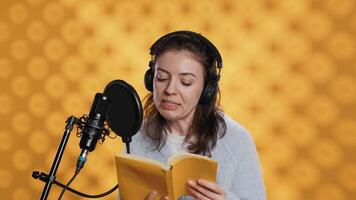 Narrator wearing headphones, reading aloud from book into microphone, exhaling after finally finishing job. Person recording audiobook, creating engaging media content for listeners, camera A video