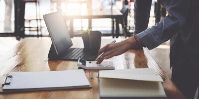 Young accountant man analyzes financial data using calculator and laptop computer to compute and summarize big data for present on conference. financial concept. photo