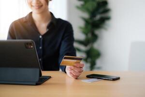 mujer en casual camisa pago con crédito tarjeta en línea mientras haciendo pedidos vía solicitud en tableta. exitoso y contento negocio mujer haciendo transacción utilizando móvil banco solicitud. foto