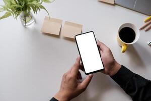 Close up of a man holding smartphone with blank screen mobile on wooden desk in home office, top view photo