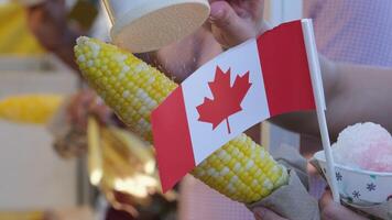 Canada Surrey Hot corn and Canada flag sprinkle salt on the corn Canada Day Families, people dressed in red, walk in the square on a holiday weekend video