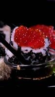 sushi met rood en zwart kaviaar detailopname van uramaki sushi broodjes met rood kaviaar, Zalm, komkommer en avocado geïsoleerd Aan een zwart achtergrond. heerlijk traditioneel Japans voedsel met sushi broodjes. video