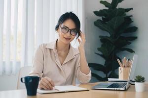 Asian Business woman sitting in office with laptop computer on wooden desk photo