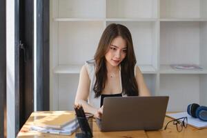 Asian Business woman sitting in office with laptop computer on wooden desk. photo