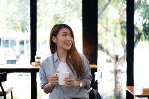 Young beautiful woman holding coffee cup and feeling fresh while sitting at her working place at monday morning. photo