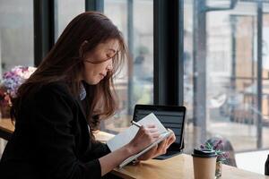 Young woman writes information from portable notebook while prepare for lectures. Female hads writing on paper notebook photo