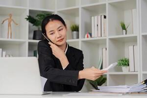 Business woman looking busy while talking on mobile and searching through document on messy table in an office photo