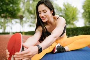 un sonriente mujer en ropa de deporte es calentamiento arriba y extensión antes de formación en el parque. sano estilo de vida concepto foto