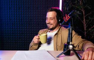 Relaxed stylish radio host in mustard shirt with headphones talking into microphone and sharing story with audience while sitting at desk in neon lit studio recording podcast photo