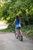 Woman riding bicycle on road in the summer park outdoors, back view photo