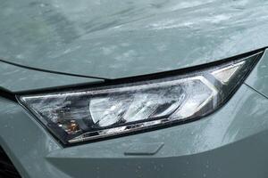 A portrait of the right headlight of a green hybrid toyota rav4 car with water drops. Kyiv, Ukraine - April 2024. photo