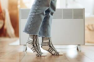 Close-up of a woman in warm socks near an electric heater at home. winter season concept photo