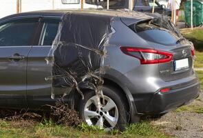 Wrecked gray crumpled car from the left side after accident with a destroyed door, after a powerful impact in parking photo
