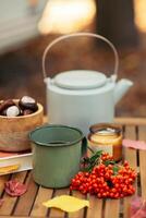 un taza de té o café y un libro en un de madera mesa en contra el antecedentes de caído hojas, otoño estación, todavía vida con hojas, un libro y viburnum y castañas en el jardín al aire libre. foto