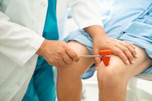 Asian doctor use hammer knock senior woman patient to check knee reflex, nerve and muscle in hospital. photo