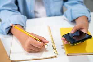 Teenage write in notebook and use mobile phone search data online to online learning university education. photo