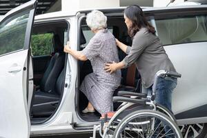 cuidador ayuda y apoyo asiático mayor mujer sentado en silla de ruedas preparar obtener a su coche a viaje en día festivo. foto