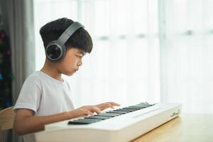 A young boy is playing the keyboard with headphones on. He is focused on the music and he is enjoying himself photo