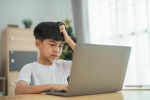 A young boy is sitting at a table with a laptop in front of him photo