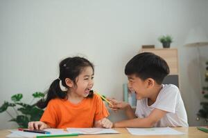 Two children are laughing and playing with pencils. One of them is holding a pencil in his mouth photo