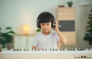 un joven niño vistiendo auriculares es sentado a un teclado. el niño es vistiendo un blanco camisa y él es enfocado en jugando el teclado foto