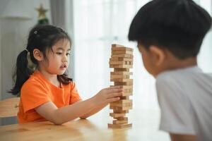 A girl and a boy are playing with wooden blocks. The girl is holding a block and the boy is watching her photo