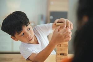 un joven chico es jugando con un de madera bloquear torre. él es enfocado en el torre y él es disfrutando él mismo foto