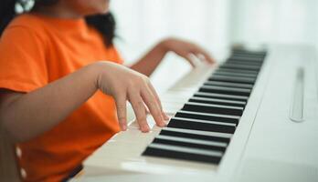 Close uo hands. Asian young girl is smiling sitting at a piano, wearing headphones. She is wearing an orange shirt. The room is filled with books and keyboard. photo