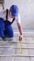 uomo lavoratore prende misurazioni durante il installazione di un' caldo pavimento. caldo pavimento riscaldamento sistema. carino soriano gatto video