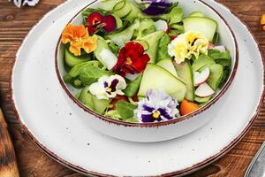Salad of vegetables and flowers on wooden background. photo
