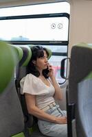 A sitting girl in transport. Vertical close-up photo. The girl is talking on the phone sitting at the window in the train car. Phone conversation. photo