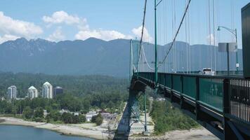 Lions Gate Bridge Car traffic, Mountains, Park Summer day Stanley Park iron structure the sun is shining, clear sky ships Pacific Ocean view of Stanley Park video