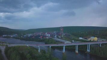 fågelöga se. klämma. se av de kväll stad med en bro över de flod, hus, bilar, skog, rör och en mörk kväll himmel med små moln. video