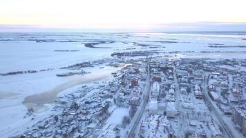 Winter view from a drone.Clip. A view of the city from a height where all the houses are covered in snow, you can see roads with cars, a frozen river and a few trees and a bright sky without clouds. video
