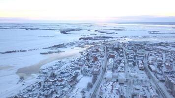 invierno ver desde un drone.clip. un ver de el ciudad desde un altura dónde todas el casas son cubierto en nieve, usted lata ver carreteras con carros, un congelado río y un pocos arboles y un brillante cielo sin nubes video