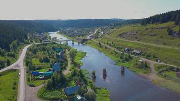 Top view of bridge over river in green valley with small town. Clip. Beautiful view of town by river with bridge in summer video