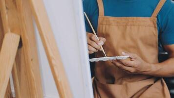 over- de schouder selectief focus schot van mannetje artiest gebruik makend van borstel terwijl toevoegen kleur verf naar potlood tekening Aan canvas video